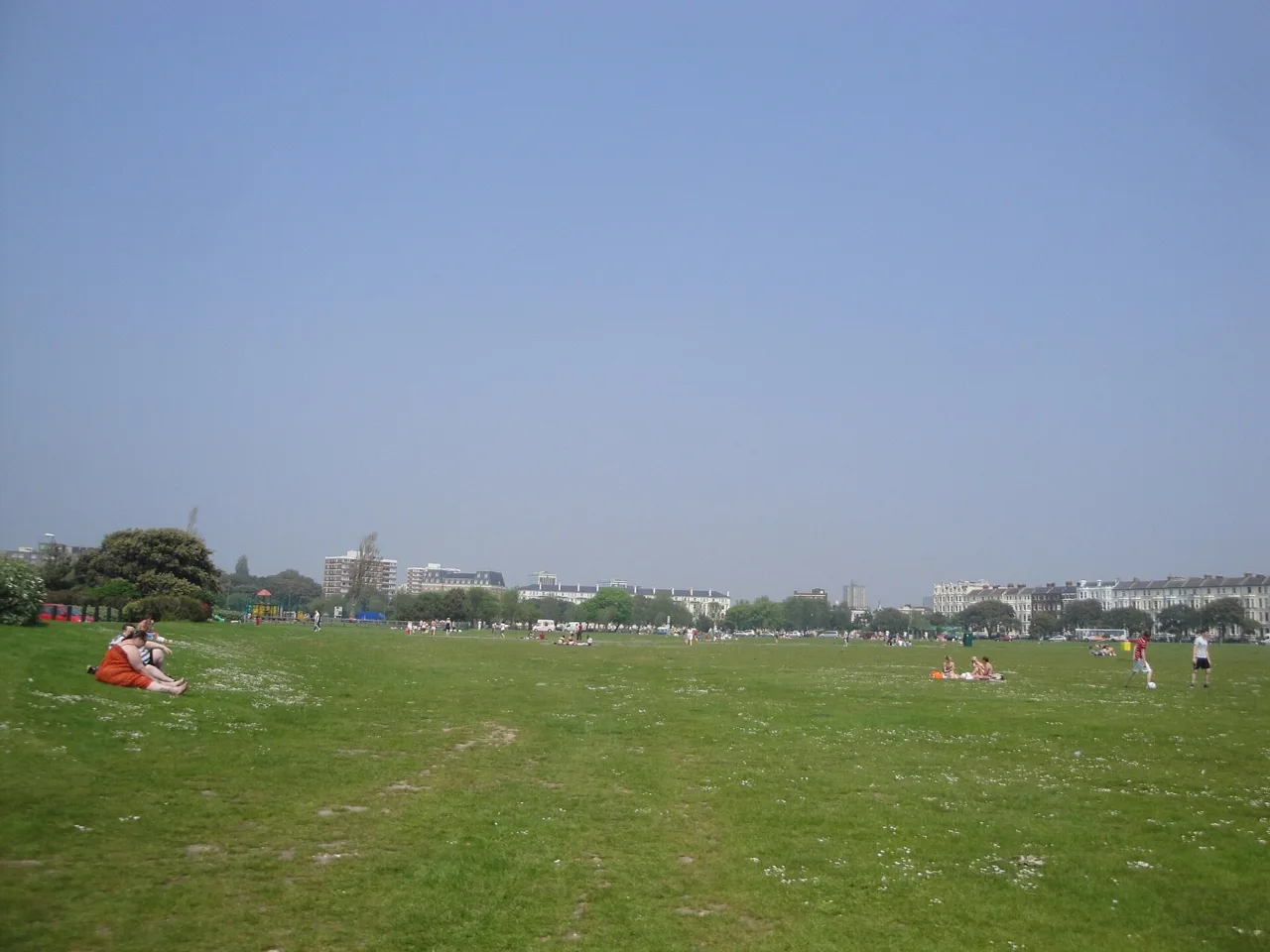 People relaxing on the broad grass of Southsea Common beneath a blue sky