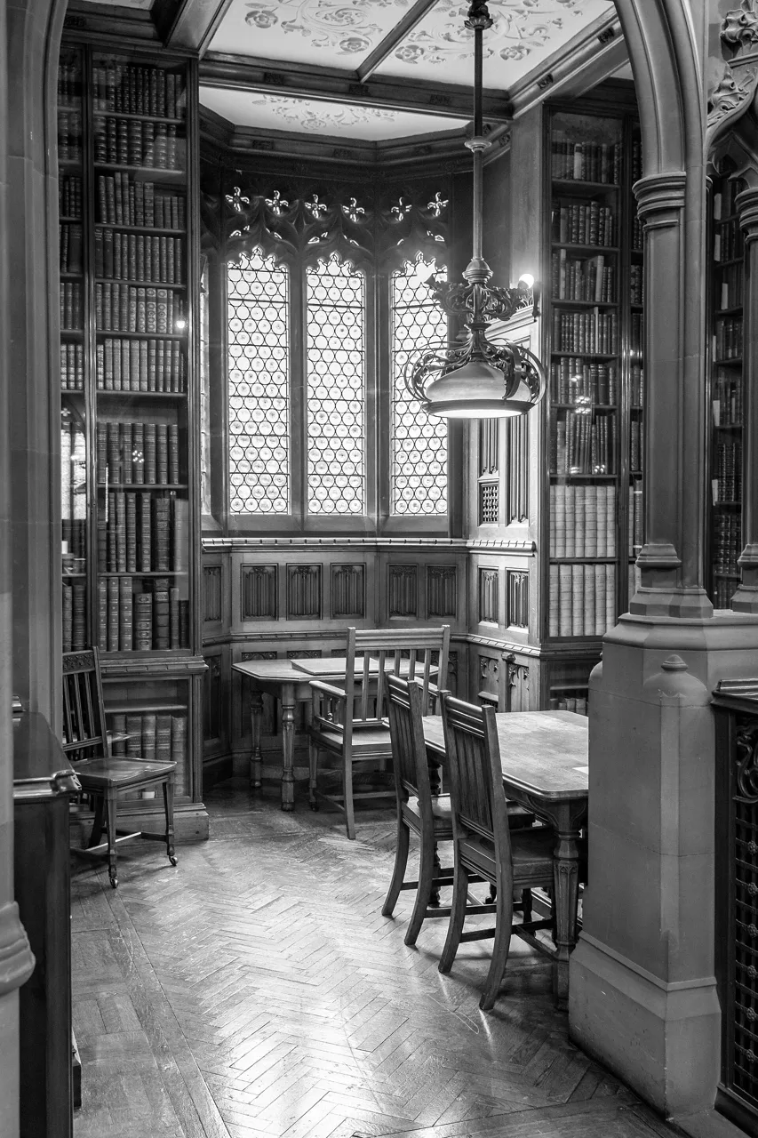Black-and-white view of bookshelves, desks and a tall window inside John Rylands Library