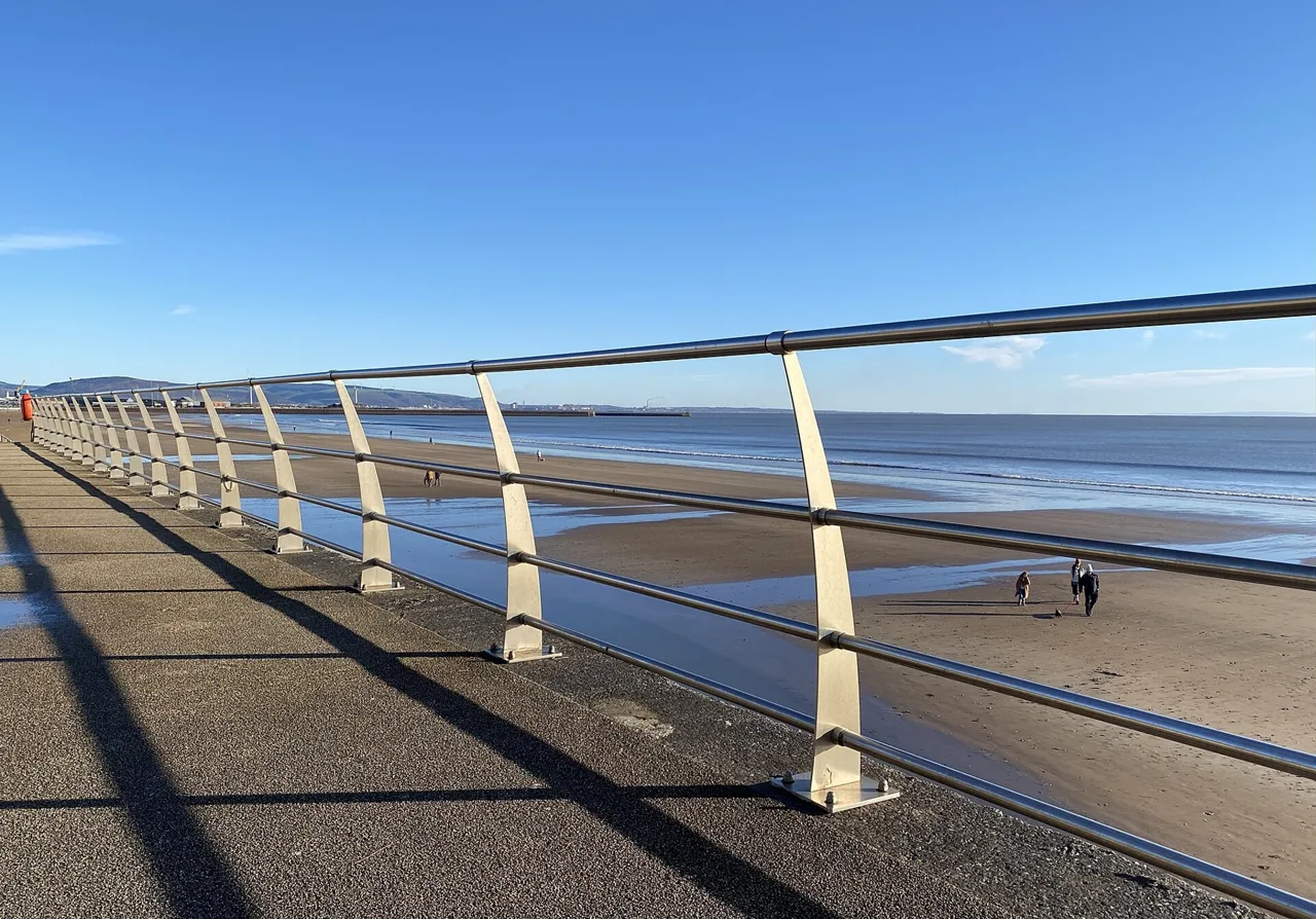 Promenade railings beside the beach and open water of Swansea Bay