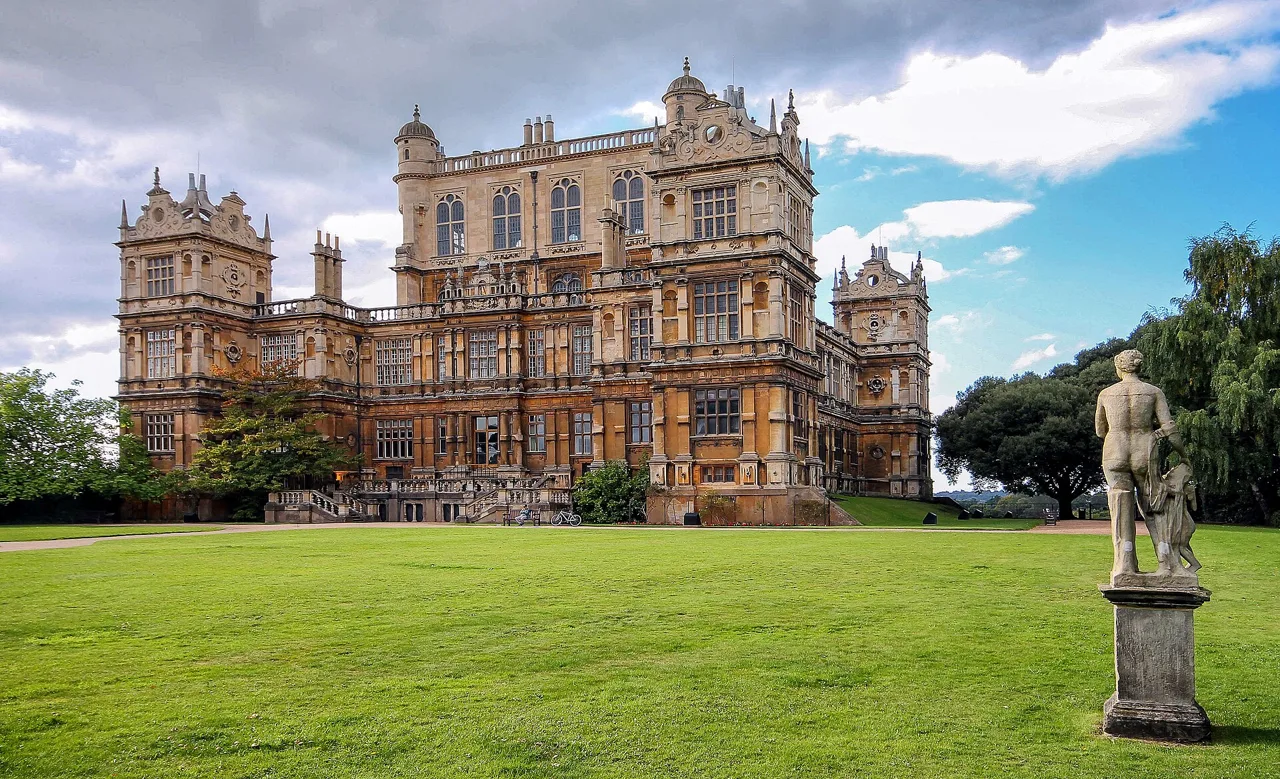 Wollaton Hall above its lawn, with a stone statue in the foreground