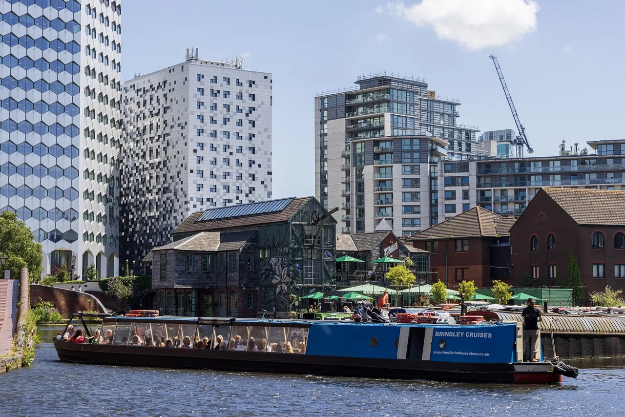 A narrowboat crossing Gas Street Basin with waterside buildings behind
