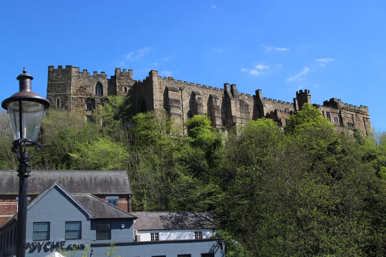 Durham Castle walls and towers rising above trees on the riverbank