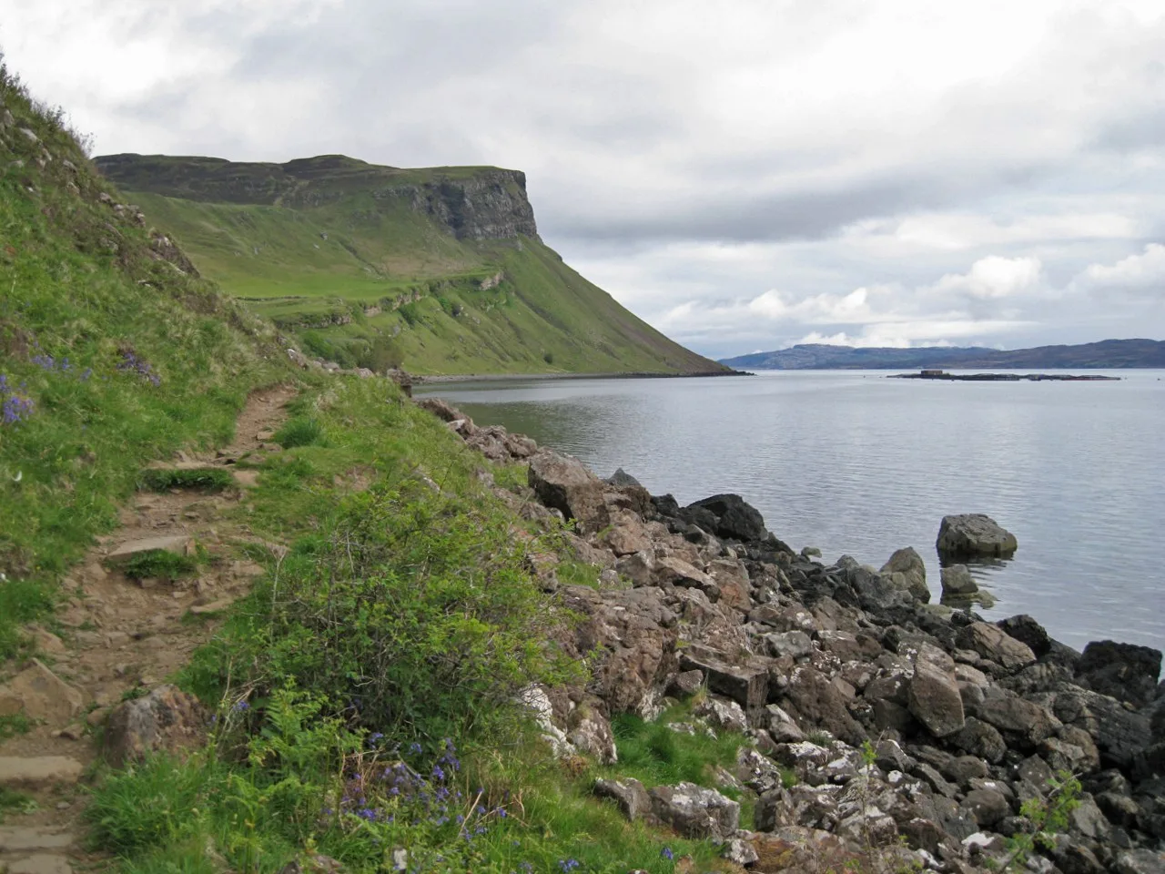 Narrow uneven Scorrybreac coastal path beside a rocky shore and green cliffs