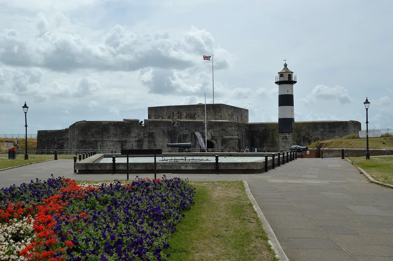 Stone walls and striped lighthouse at Southsea Castle beyond a flower bed