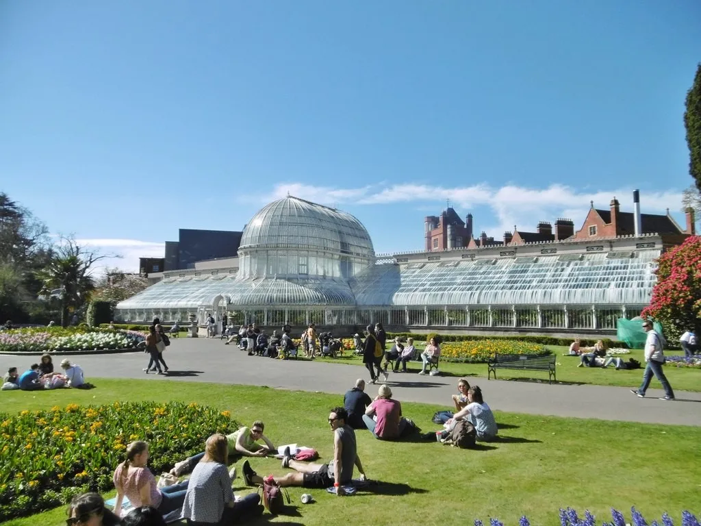 The curved glass Palm House overlooking visitors and flower beds in Belfast