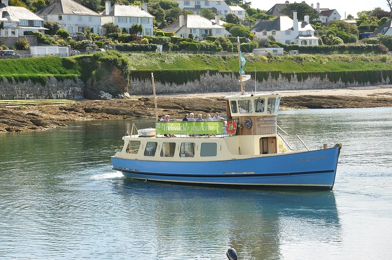 Blue and cream St Mawes passenger ferry on the water beside the village shore