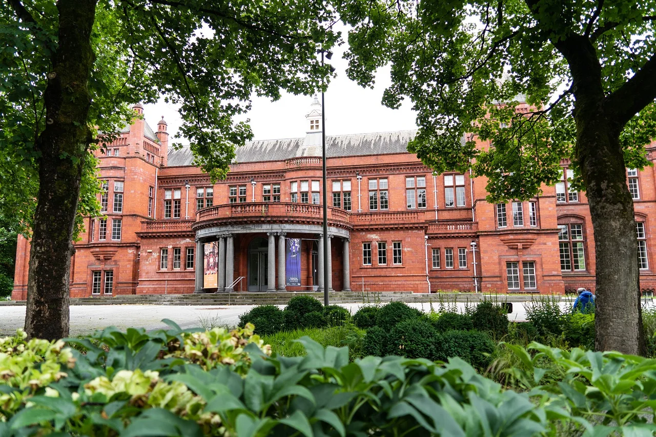 Red-brick facade of the Whitworth framed by green trees and planting