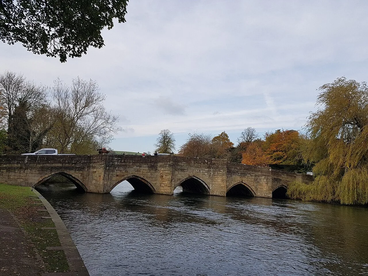Stone arches of Bakewell Bridge over the River Wye with autumn trees beside the water