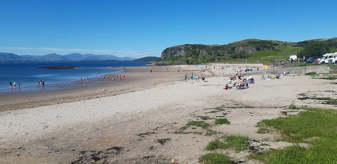 Wide sandy beach at Ganavan Sands with visitors and hills beyond