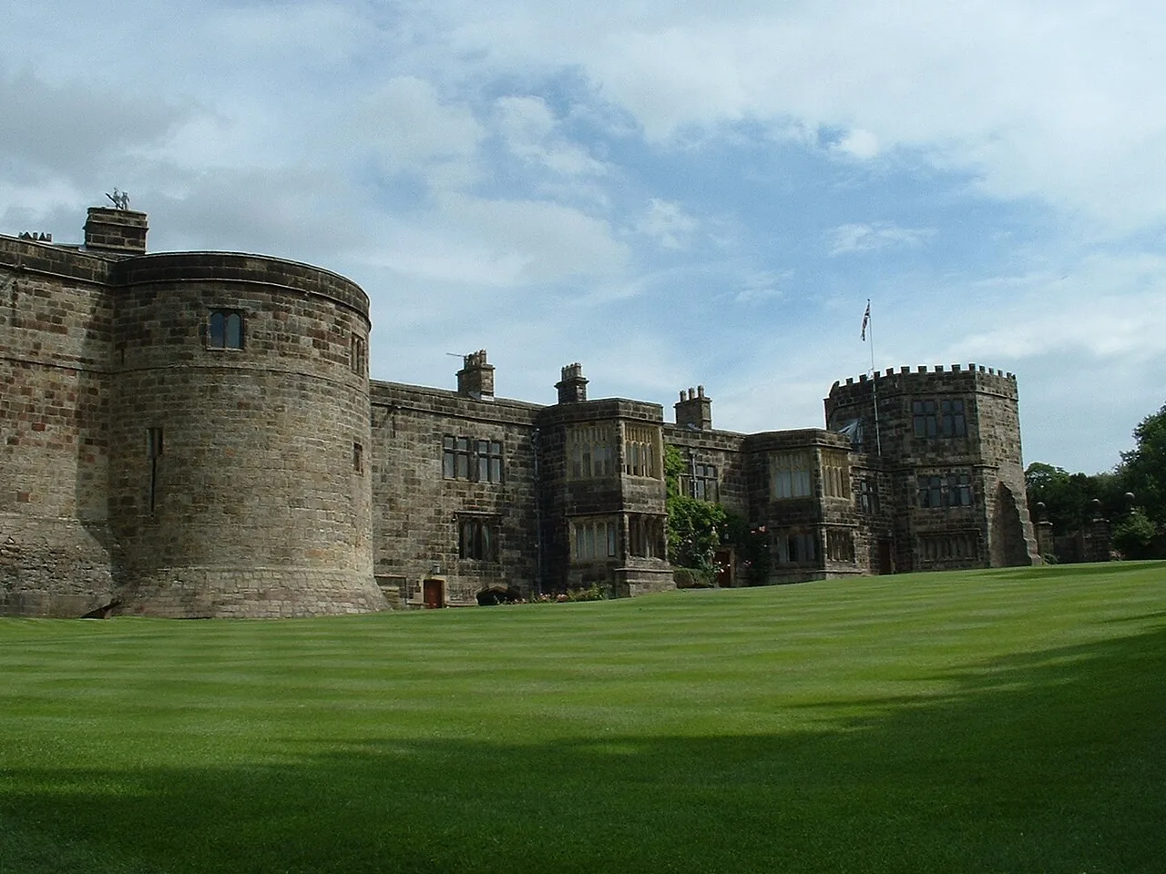 Stone towers and the main range of Skipton Castle above a green lawn