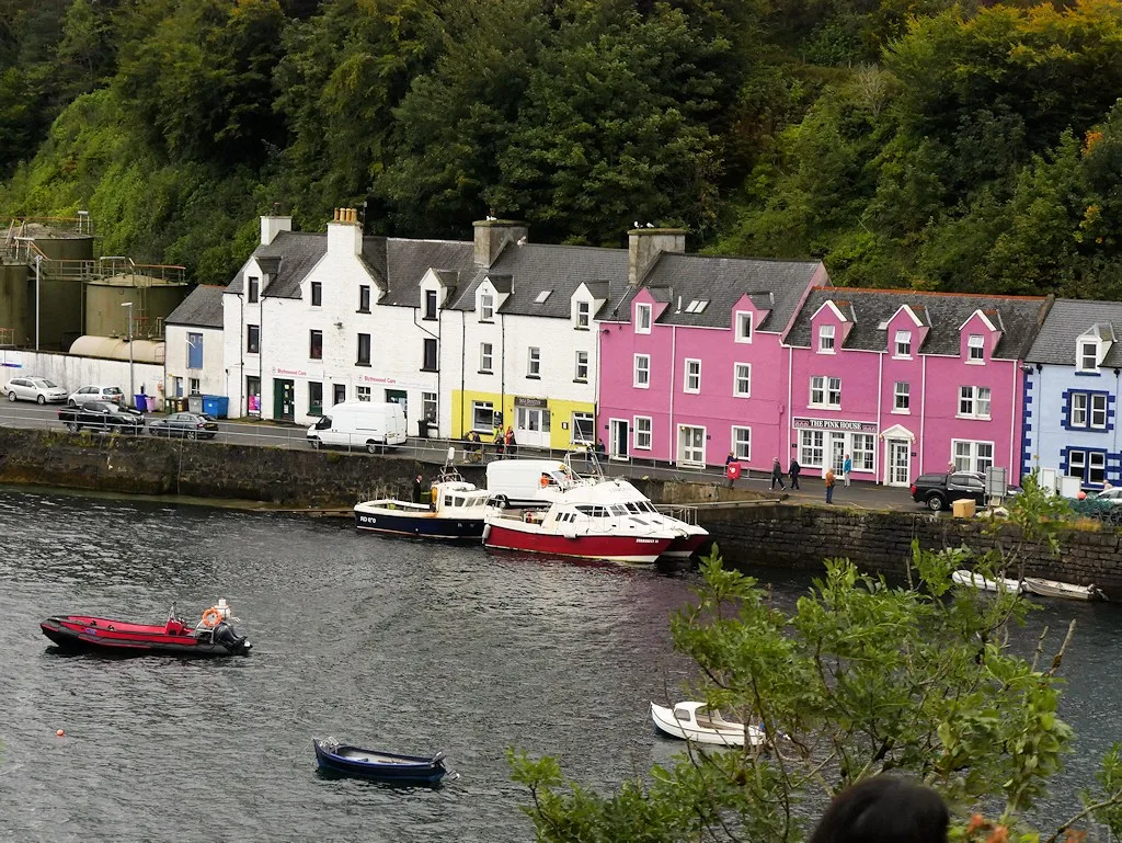 Pink, white and blue buildings above the quayside and moored boats at Portree Harbour