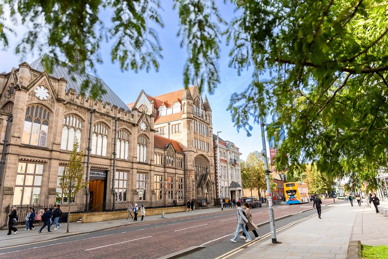 Manchester Museum’s stone facade on Oxford Road beneath leafy branches